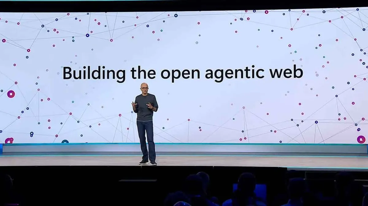 Mees räägib laval suure ekraani ees, millel on tekst 'Building the open agentic web'. Ekraanil on ka värvilised punktid ja jooned moodustamas võrgustiku mustrit.