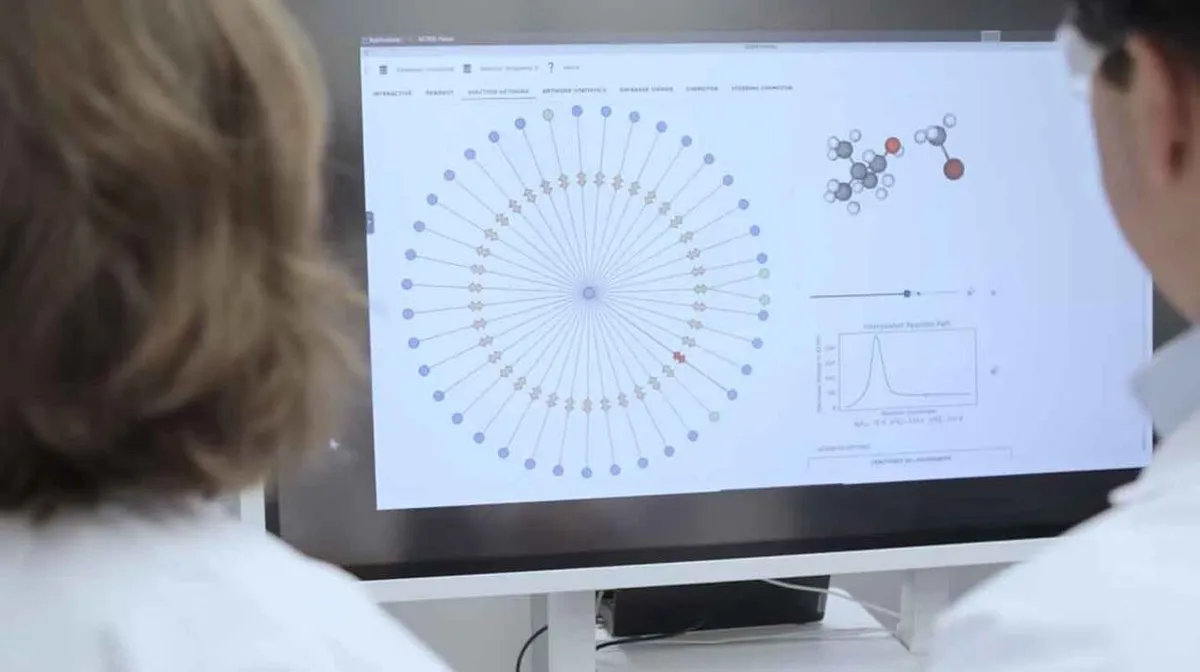 Kaks inimest vaatavad arvutiekraani, millel kuvatakse graafik, molekulide struktuurid ja diagramm. Ekraanil on kujutatud keerukas diagramm koos erinevat värvi punktidega ja molekulide 3D-kujutis. Alumises paremas nurgas on joonis koos tekstiga.