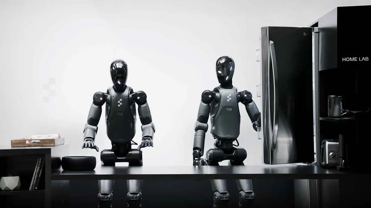Kaks humanoidset robotit istuvad laua taga. Paremal olev robot avab külmkappi, mis on nende kõrval. Taustal on näha riiulit ja erinevaid esemeid.