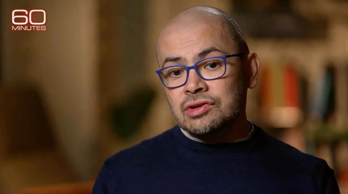 Pildil on mees, kes kannab prille ja tumesinist kampsunit. Ta on keskendunud ja taust on hägune. Ülesse vasakule on kirjutatud '60 MINUTES'.